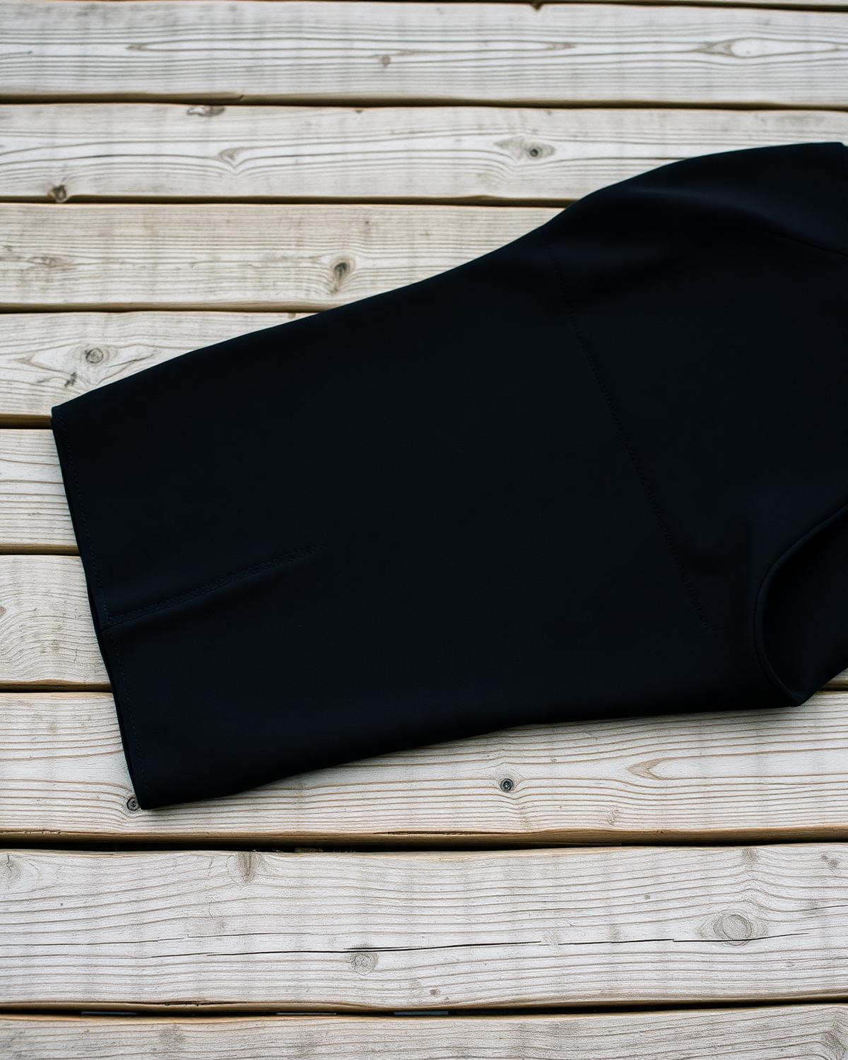 Brightonkelp Mariner cold-water wetsuit 4/3mm in deep black neoprene, laid flat on weathered Brighton beach planks at low tide